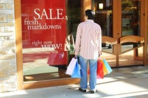 A young man carrying shopping bags looking at sale sign at an outdoor shopping mall