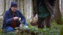 Zwei Männer mit Körben finden in einem Wald menschliche Knochen.