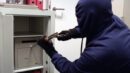 Ein dunkel gekleideter Mann mit Kapuze versucht mit Hammer und Meißel einen Tresor zu öffnen.