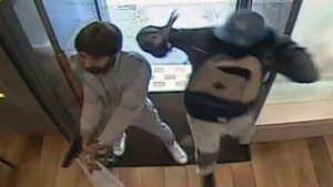 Ein Mann mit Pistole und ein Mann mit Hammer in der Tür eines Juweliergeschäfts.
