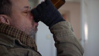 Ein obdachloser Mann trinkt aus einer Flasche Bier.