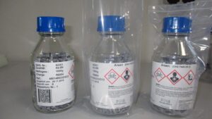 Fläschchen mit Arsengranulat. Darauf die Warnzeichen „Giftig“, „Gesundheitsschädlich“ und „Umweltgefährlich“.