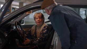 Eine im Auto sitzende Frau blickt schockiert zu ihrem Mann, der in der Fahrertür steht.