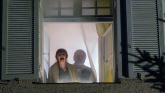Ein älteres Ehepaar steht am Fenster und ruft aus einem verrauchten Zimmer heraus um Hilfe.
