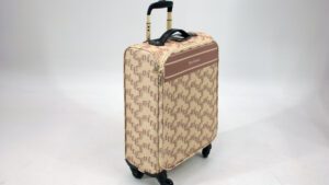 Ein Rollkoffer der Marke „Juicy Couture“. Er ist beige und hat ein braunes Muster, dass aus dem Logo der Marke besteht.