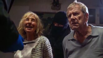 Zwei maskierte Männer bedrohen ein altes Ehepaar mit Messern.
