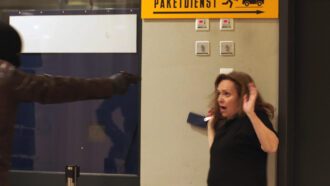 Ein maskierter Mann mit Lederjacke richtet seine Pistole auf eine Angestellte eines Supermarktes.