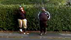 Zwei Männer in Jogginghose stehen vor einer Hecke.