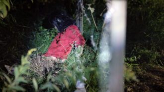 Ein kleines dunkelhaariges Mädchen mit rotem Pulli lehnt am Pfosten eines Weidezauns. Ihr Blick ist nach unten gerichtet. Sie ist tot.