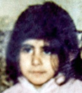 Zeynep hat dunkle Haare, schulterlang und ein Pony. Sie trägt ein weißes Kleid.