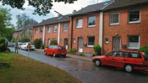 Mehrere Reihenhäuser mit Backstein-Fassade. Auf der Straße vor den Häusern stehen Autos