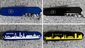 Vorder- und Rückseite von zwei Taschenmessern. Eines in blau mit dem Panorama von Bochum in weiß auf der Rückseite. Das andere in schwarz mit gelbem Dortmund-Panorama.