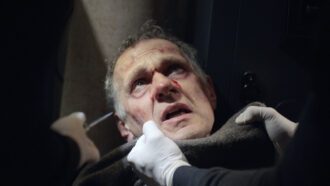 Ein blutender Mann wird von einem Unbekannten am Kragen gepackt. Ein zweiter Unbekannter hält ihm ein Messer vors Gesicht.