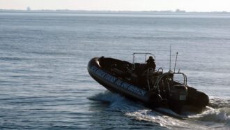 Ein Schlauchboot mit Außenbordmotor und einem Mann am Steuerrad fährt Richtung offener See.