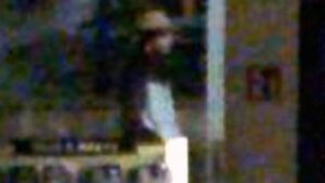 Durch ein Ladenfenster sieht man einen Mann in einem weißen Anorak mit schwarzer Brustpartie und Ärmeln.