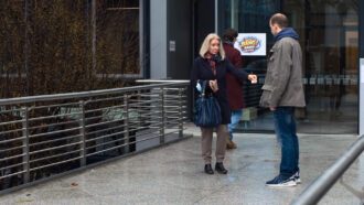 Eine Frau und ein Mann stehen sich gegenüber. Sie gibt ihm einen Zettel.