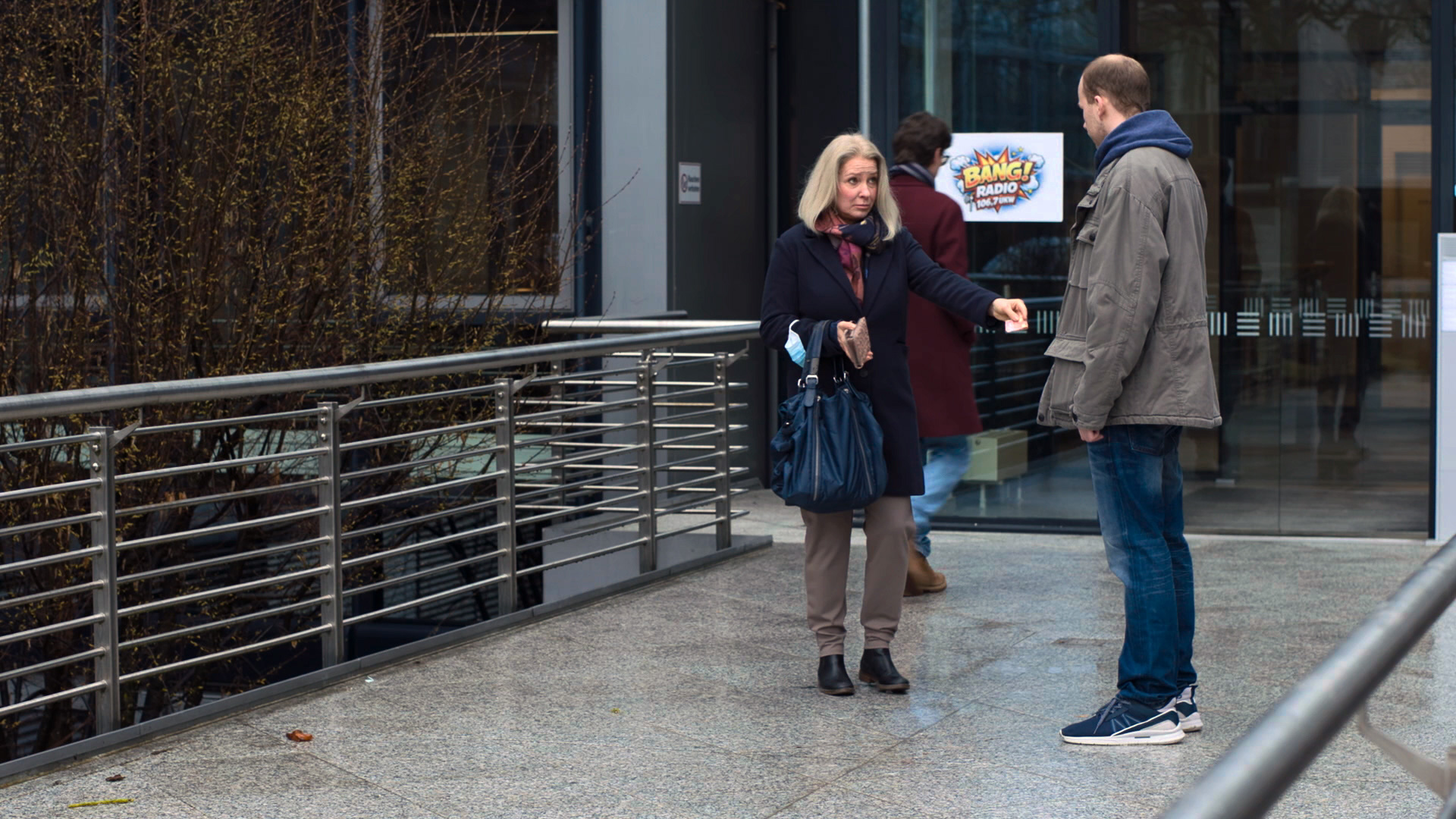 Eine Frau und ein Mann stehen sich gegenüber. Sie gibt ihm einen Zettel.