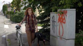 Jutta Schulz geht mit ihrem Hund und ihrem Fahrrad die Straße entlang.