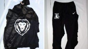 Eine schwarze Trainingsjacke mit weißem Löwenkopf auf dem Rücken und eine Trainingshose mit dem weißen Buchstaben „L“