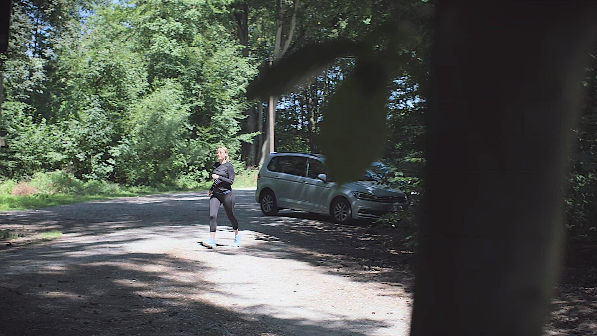Eine Frau in Sportkleidung joggt auf einem Parkplatz im Wald.